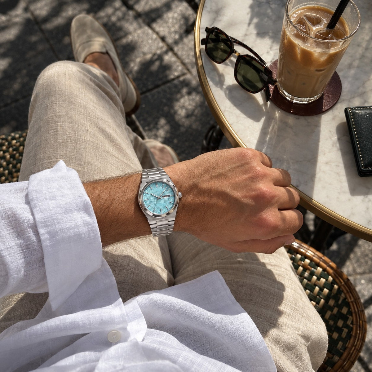 Norentime Guilloche watch with turquoise dial on a man's wrist at a café